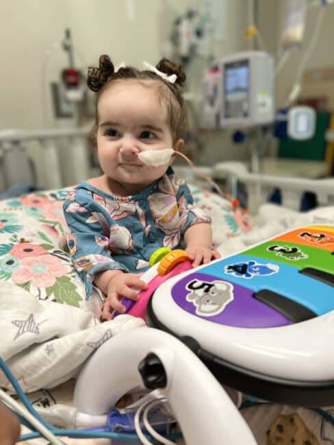 A young child sits in a hospital bed, playing with a toy piano.