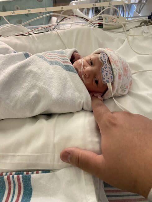 A newborn baby holding an adult's finger