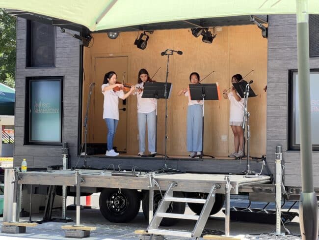Four young girls play violin on a stage.
